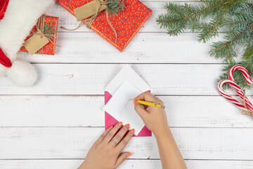 The young girl written letter to Santa Claus and puts them in an envelope, flat lay. Christmas decorations and gift box on wooden desk, top view. Concept of New Year eve.