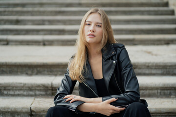 Fototapeta premium portrait of a young female model blonde Caucasian appearance, posing for the camera open face, straight hair. she is wearing a black leather fashionable stylish jacket