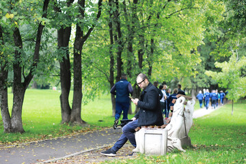 A young man in glasses walks in the park with an umbrella during the rain.