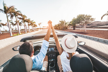 Romantic couple enjoying holidays driving a convertible car on the road at sunset. People rent car...