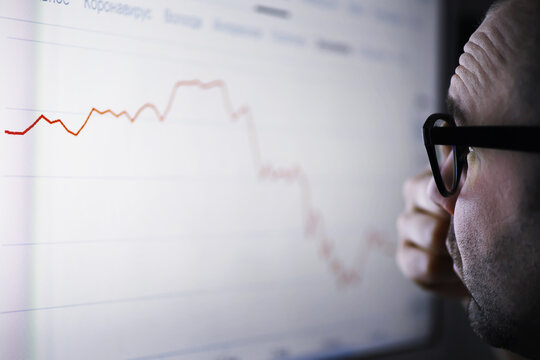 A businessman is looking at a graph on a monitor. An exchange broker evaluates stock market trends. A man with glasses in front of a curve of the dynamics of the economy.