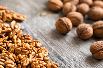 Heap of fresh walnut kernels and whole walnuts on wooden table - natural pattern background detail. Close up of brown surface texture. Healthy organic food, BIO viands, back to nature concept
