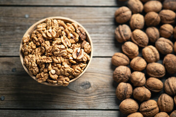 Fresh walnut kernels and whole walnuts in a bowl on rustic old wooden table. Healthy organic food, BIO viands, natural background. Copy space for your advertising text message