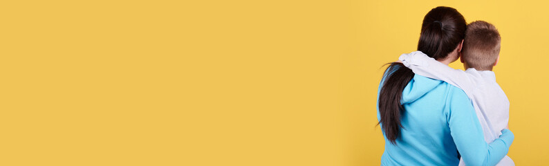 Brunette boy and mother sitting together, hugs, love, family. Isolated on yellow background, copy...