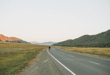 Young woman on skateboard on the road against beautiful mountain landscape, Chuysky tract, Altai