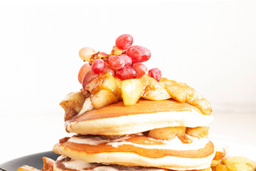 Stack of delicious pancakes with fried caramelized apples, grapes and sour cream.
