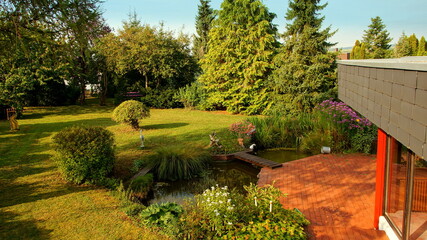 moderner Bungalow mit schöner Terrasse am Teich mit  Holzbrücke und herbstlichen Garten	
