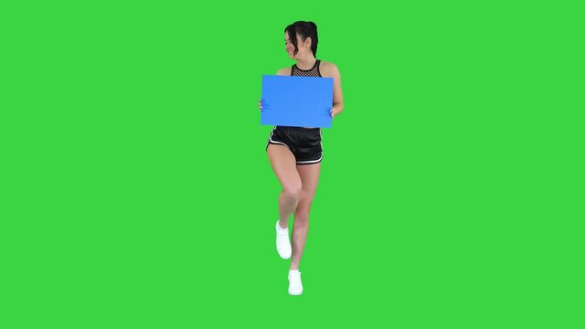 Charming girl holding empty board and dancing on a Green Screen, Chroma Key.