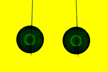 Green Natural Plastic Round Plane Bottle Cap Pendulum Hanging On Stick Against Isolated Yellow...