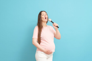 happy young pregnant woman in pink t-shirt singing into the microphone on blue background