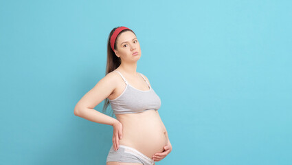 young pregnant woman on blue background, backache, big heavy belly pregnant