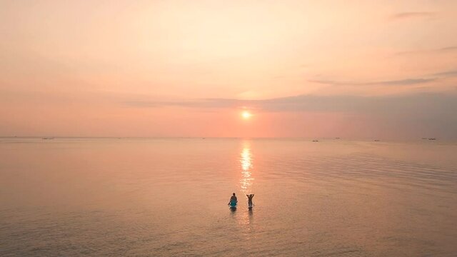 Two young women enjoying an incredible orange sunset in the ocean. 