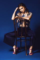 Woman in pants and floral silver top sitting on wooden chair