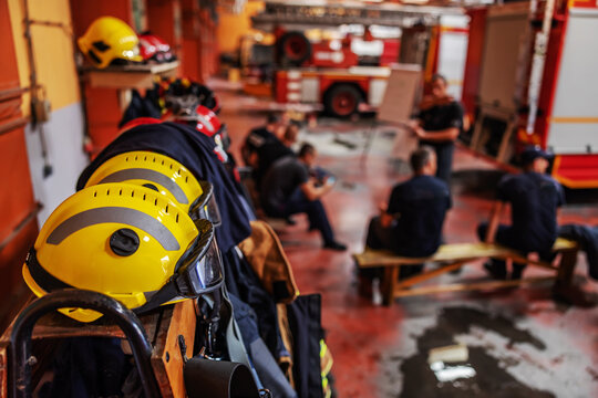 Picture of protective suit and helmets in fire brigade. In background are firemen.