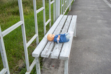 Children's toy doll in dress and pants lies forgotten on a wooden bench