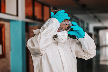 Worker in sterile white uniform taking off goggles while standing in hallway in school after disinfecting.