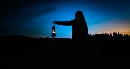 Silhouette of a woman looking into the last light of the day by a lake in the wild, holding a lit...