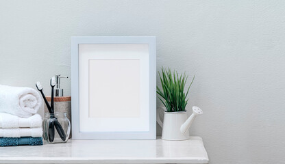 Mockup white wooden picture frame with clean towels, toothbrush  and houseplant on white wooden top table.