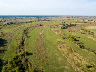 Dirt road among green meadows. Summer sunny day. Aerial drone view.