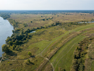Fototapeta na wymiar Dirt road among green meadows. Summer sunny day. Aerial drone view.