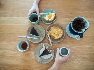 Variety of sweet bakery dishes on wood table ,two hands hold cup of beverage from opposite side.Top view,Concept for food bakery and cafe.