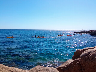 Personas practicando kayak en el mar en un dia soleado sin nubes en el cielo y el mar en calma des...