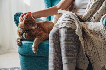 Young woman sitting in a cozy armchair, with a warm blanket, with cat