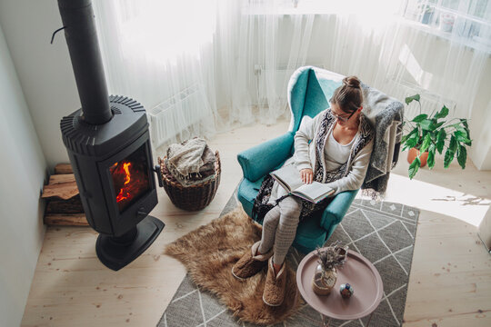 Woman Sitting In A Cozy Armchair With A Warm Blanket Reading A Book