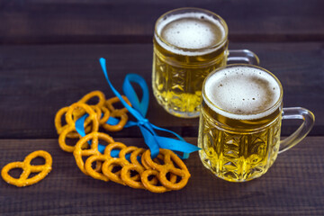 October fest concept. Beer mug with snacks of salt pritzels, bretzel and blue tape on dark wooden background. copy space