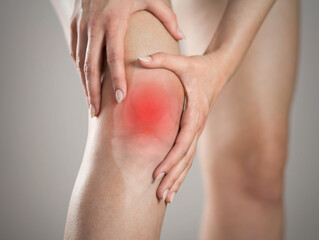 Pain in the knee of a woman. Highlighted in red. On a gray background. Close up