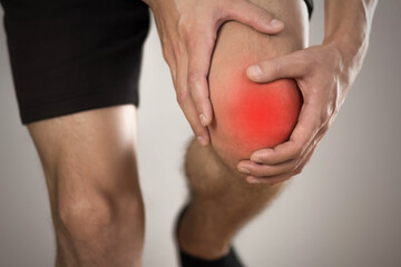 Pain in the knee of a man. Highlighted in red. On a gray background. Close up