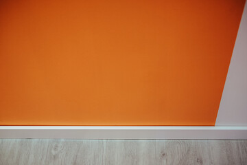 Closeup of an orange wall  and a white baseboard
