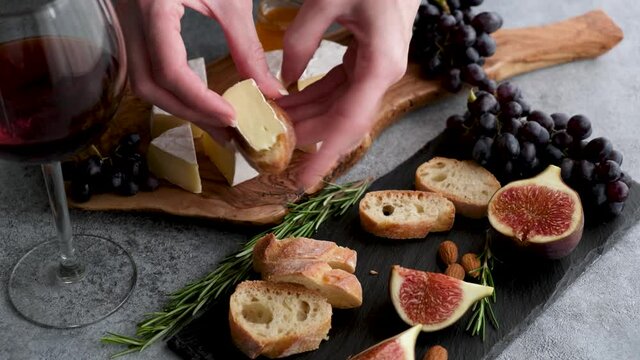 Cheese and wine appetizer plate. Female hands making finger food sandwich of baguette and slice of camembert cheese