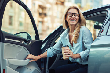 Happy attractive woman or business lady wearing eyeglasses holding cup of coffee and getting out of...
