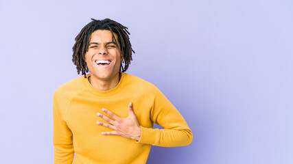 Young black man wearing rasta hairstyle laughs out loudly keeping hand on chest.