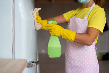 Professional house cleaning. A maid girl in the same rubber gloves and an apron wipes the refrigerator. Cleaning service and houskeeping