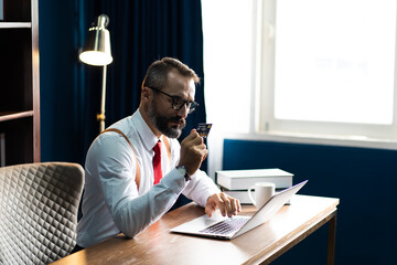 happy confident caucasian Bearded man doing online shopping with laptop and credit card sitting on desk at home office.