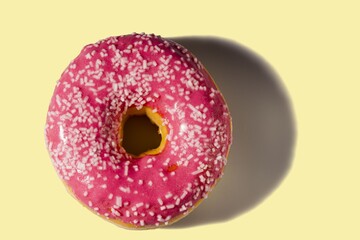 Close up view of donut sprinkled with white glaze isolated on yellow background. Food and drink concept.