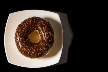 Close up view of chocolate donut  on white plate and black background. Food and health concept.