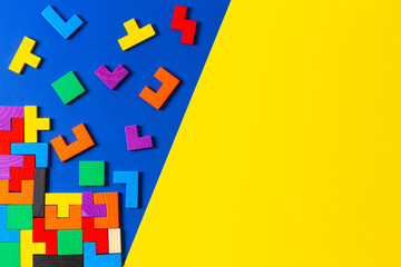 Different colorful shapes wooden puzzle blocks on blue and yellow background. Geometric shapes in different colors, top view