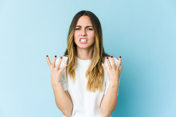 Young caucasian woman isolated on blue background upset screaming with tense hands.