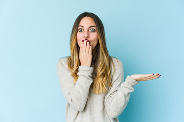 Young caucasian woman isolated on blue background impressed holding copy space on palm.