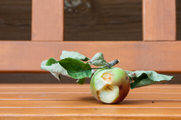 Apple with bite marks on a wooden bench in the garden. Bitten apple with leaves on a wooden background. Organic food.