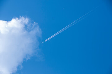 White airplane and its vapour trails on the background of a bright blue sky. Looking up at the sky. Plane flying high in the sky.