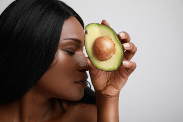 Close-up portrait of afro young woman with avocado, healthy lifestyle. Posing over white background.