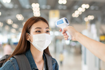 Asian female travel passenger wearing medical protective mask measure temperature with thermometer infrared scan at airport. medical healthcare for airline business during Coronavirus pandemic