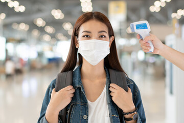 Asian female travel passenger wearing medical protective mask measure temperature with thermometer infrared scan at airport. medical healthcare for airline business during Coronavirus pandemic