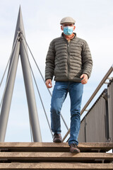 Mature man with face mask walking over a footbridge in a city