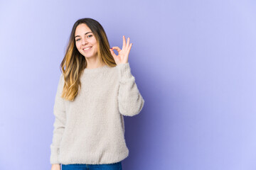 Young caucasian woman isolated on purple background cheerful and confident showing ok gesture.