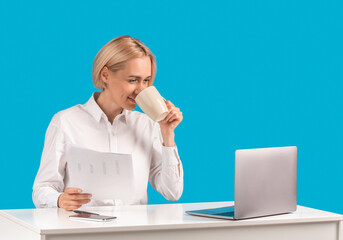 Happy female secretary with documents, coffee and laptop at workplace over blue background, copy...